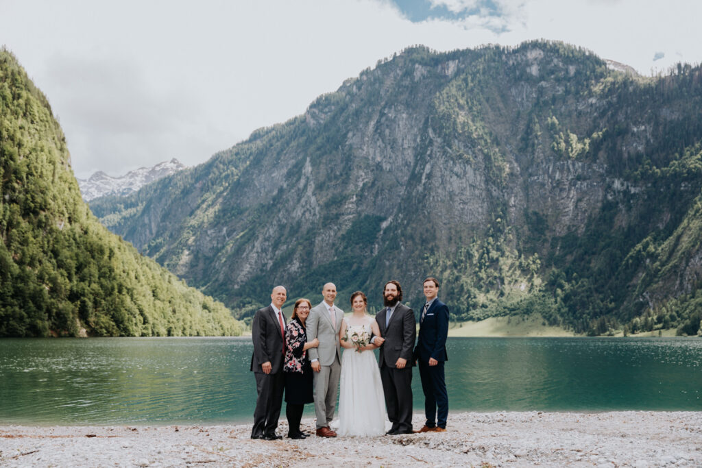 A couple who eloped in Germany stand near the Königsee with their family after their outdoor wedding ceremony