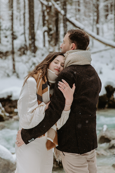 A wedding couple share a calm embrace as snow falls around them on a winter day in the Dolomites