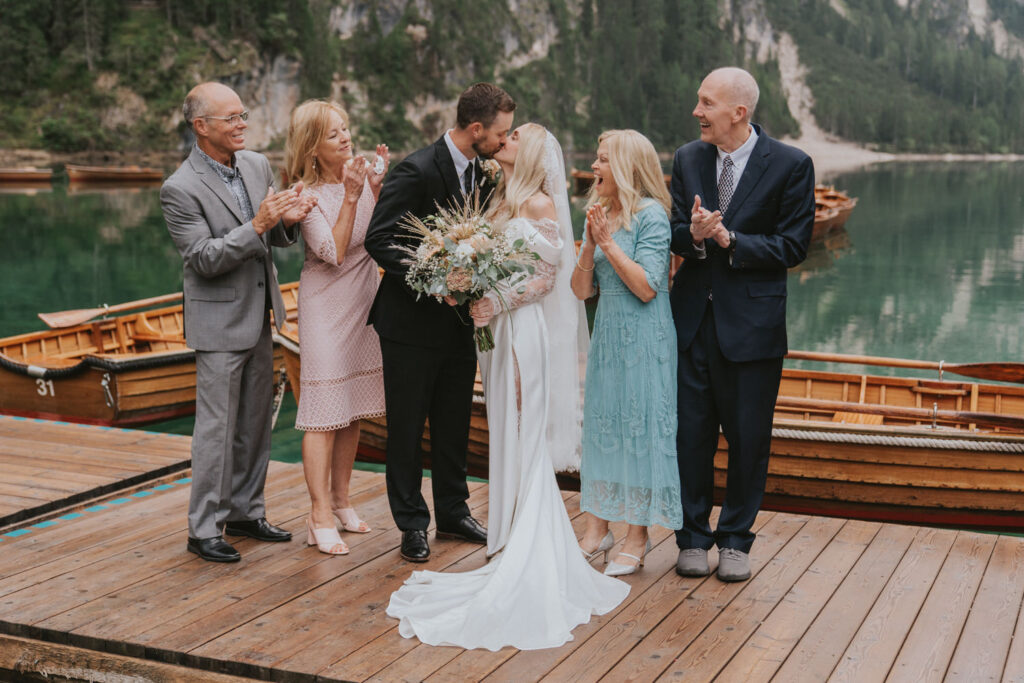 A family dressed in formal wear and wedding attire cheers on an eloping couple during their Lago di Braies wedding ceremony