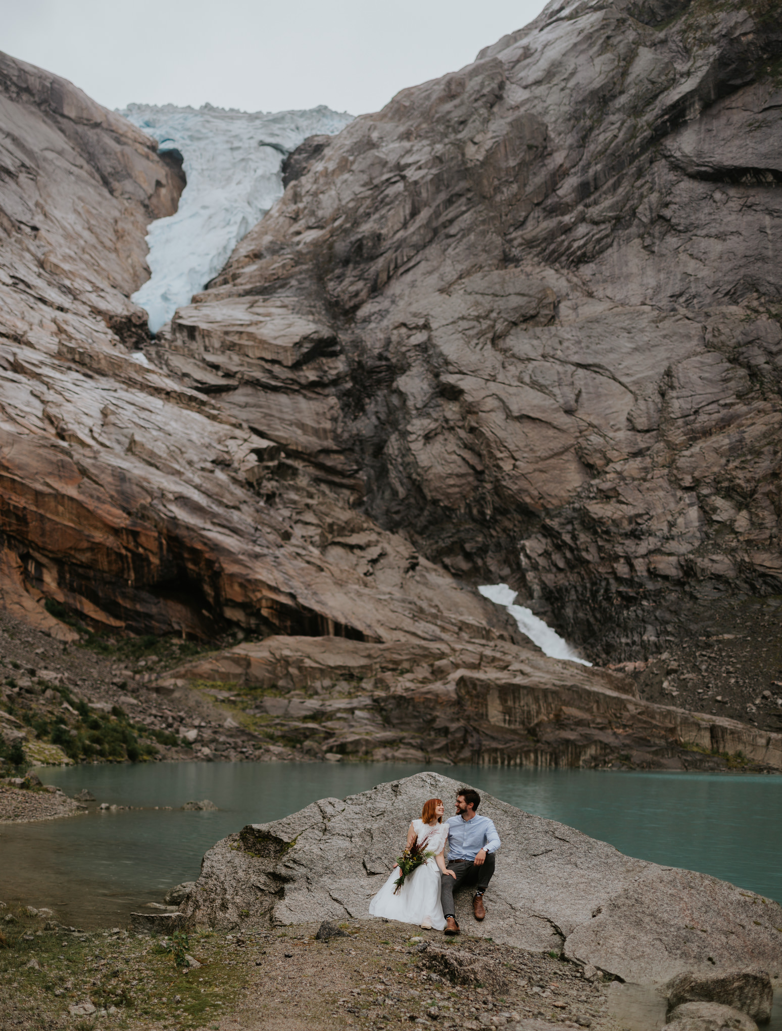 A wedding couple eloping in Norway sit under a glacier near Loenfjord
