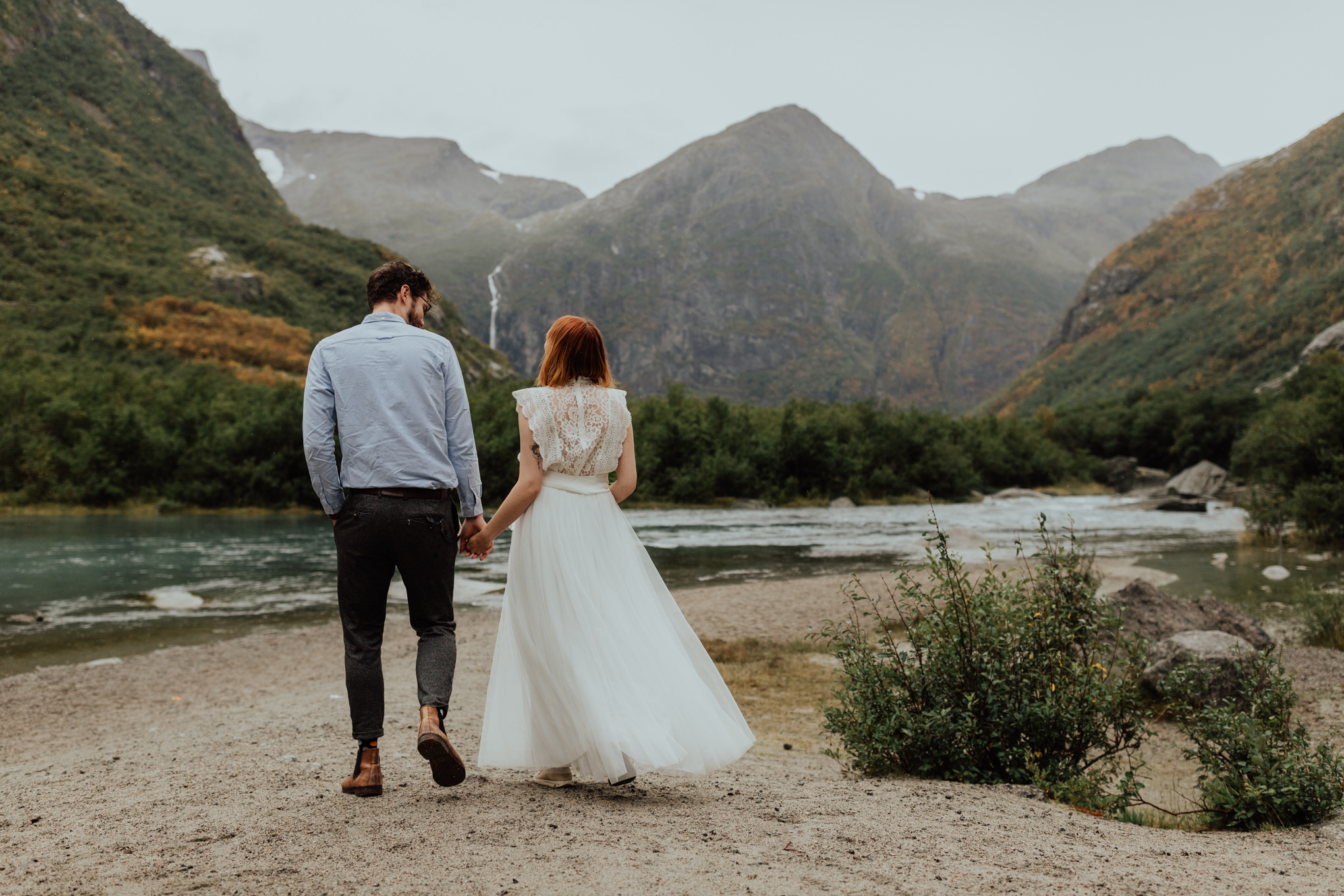 Couple eloping in Norway walk toward a waterfall during fall