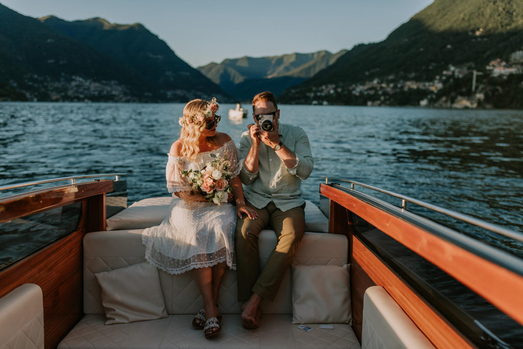 A couple sits on the back of a boat on Lake Como, photographing each other with a polaroid for their June elopement day