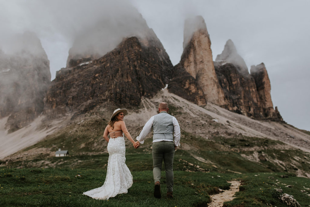 couple wearing their wedding attire in the Dolomites during their elopement, facing dramatic rocky peaks