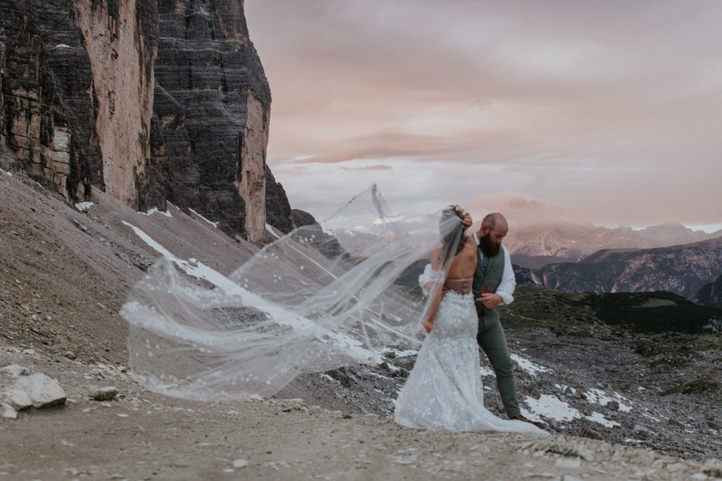 A bride holds her veil in the wind near the Tre Cime view point during their Dolomites elopement