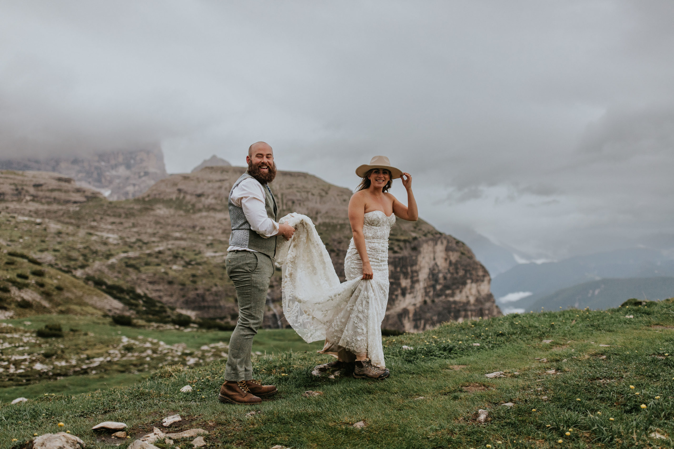A husband and wife laugh during their Dolomites elopement as they walk along a grassy trail near Tre Cime