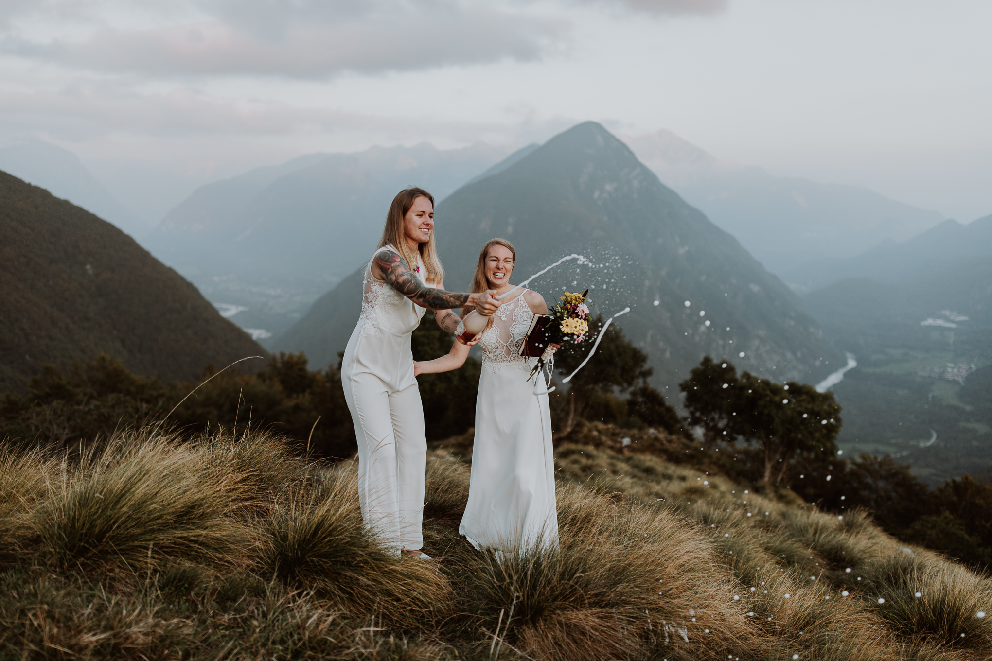 A couple laughs and smiles as they pop champagne on a mountain top in Slovenia for their wedding