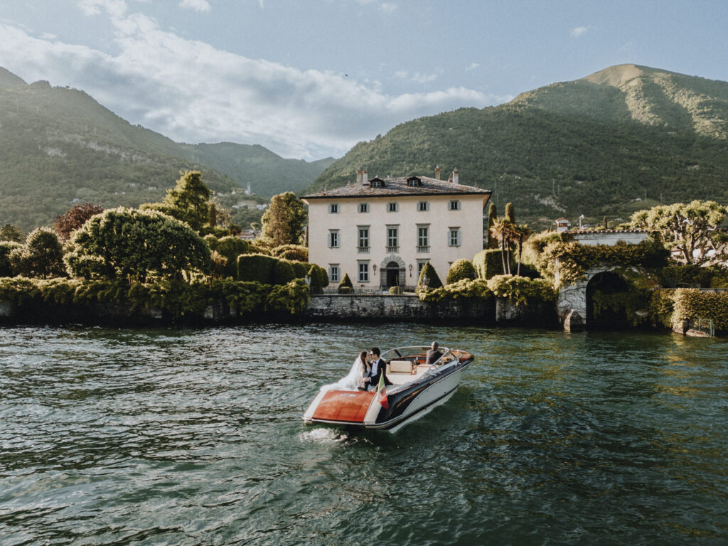 A wedding couple lounges on the back of a wooden boat in front of Villa Balbiano, lake Como, during their wedding photos