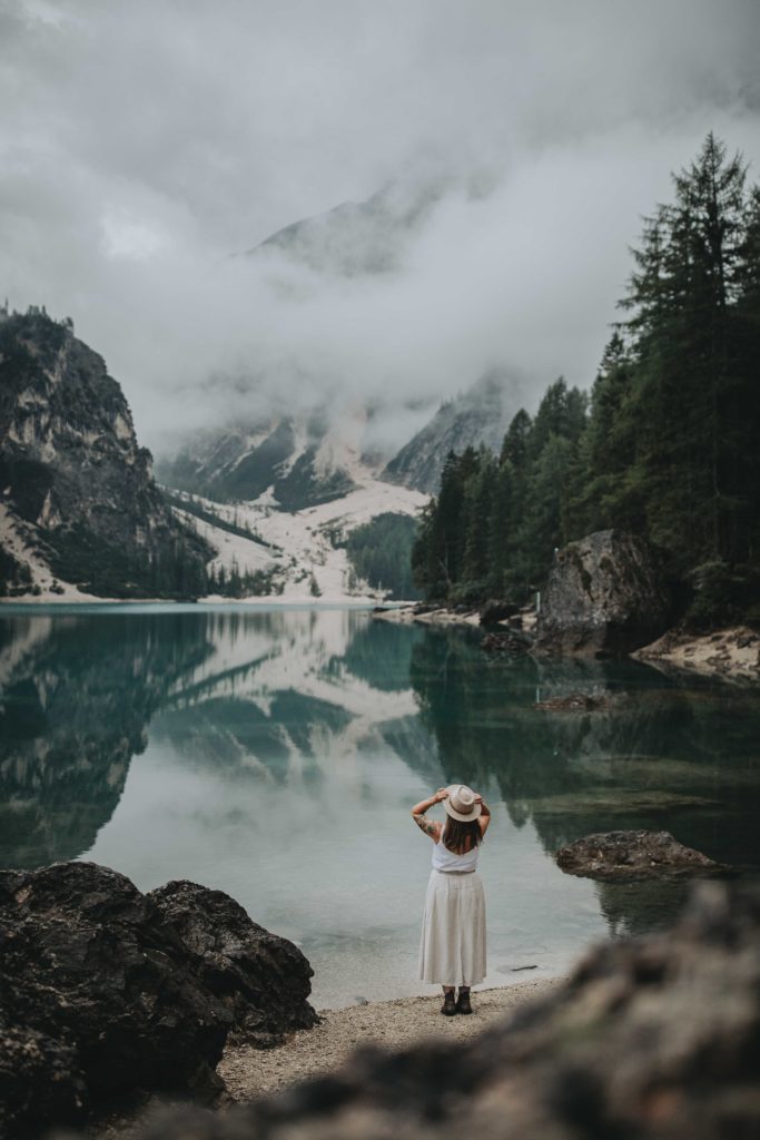 a young woman in a beige outfit and wide brim hat explores Lago di Braies in the Dolomites