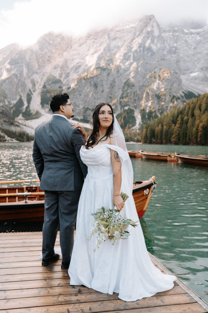 A couple pose for their elopement photos in the Dolomites wearing a white wedding dress and grey suit.