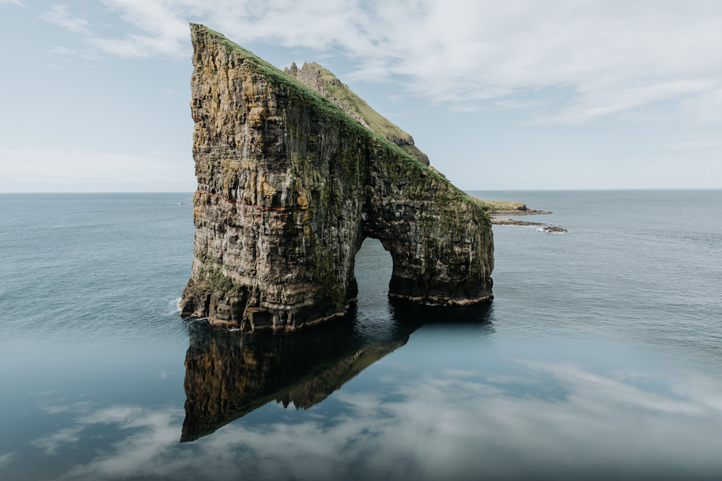 This is a photo of the Drangarnir sea stacks at the end of the Dranganir hiking trail in the Faroe islands. It is a pointy stone pillar jutting out of the ocean with a door shaped hole in the center.