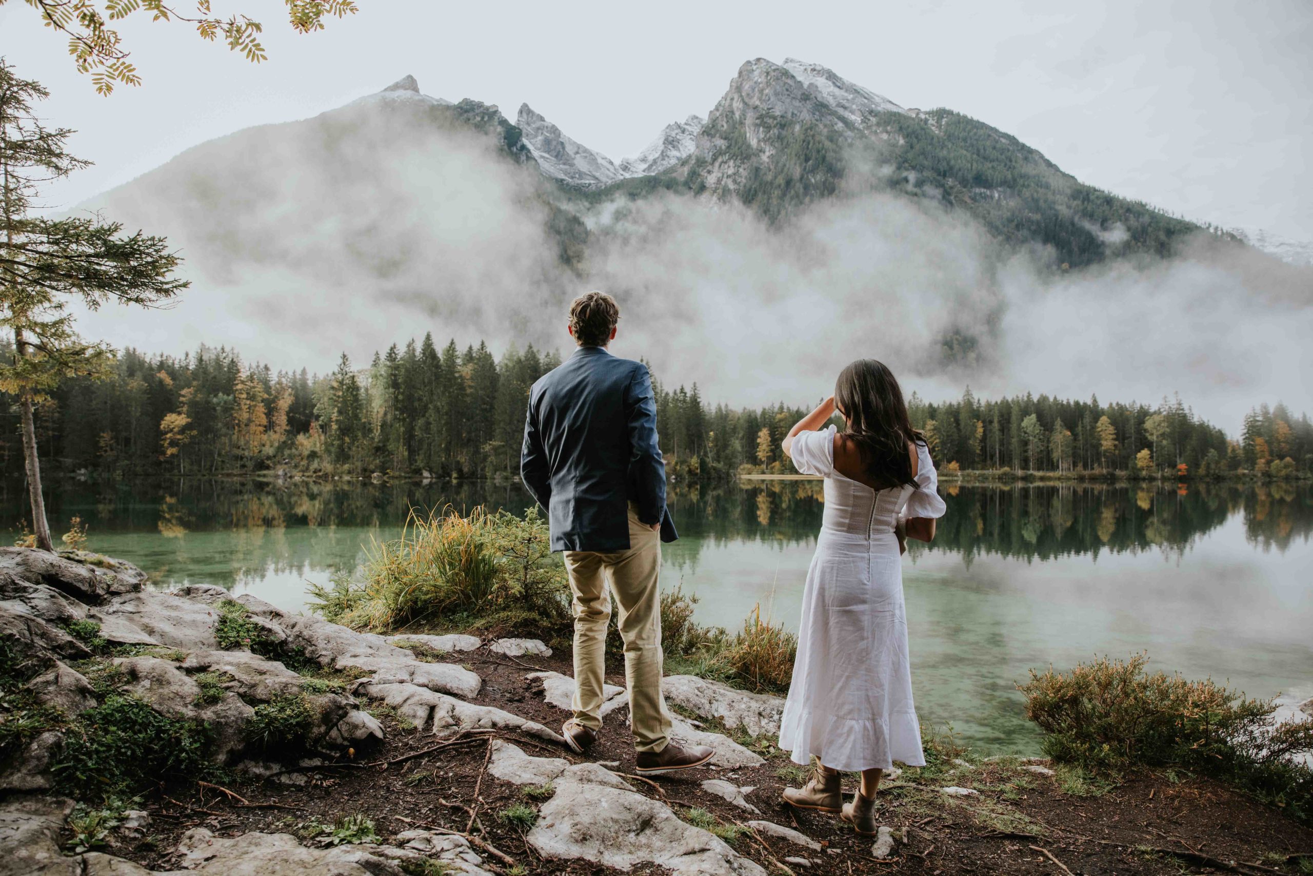 Couple stands staring over the Hintersee during their Berchtesgaden, Germany elopement photos. They both have their backs to the camera.