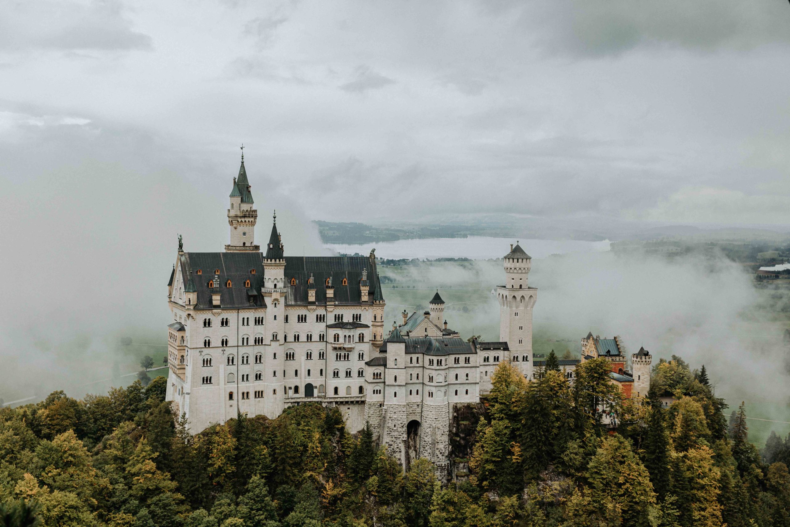 A great place to elope in Germany is Schloss Neuschwanstein. This photo of the castle is from the side with the area of Füssen in the background. The castle is surrounded by mist and the leaves are changing color for fall.