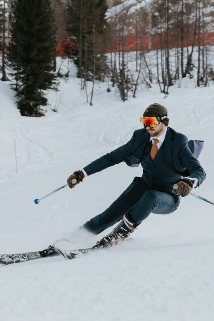 A man skis down the slopes wearing his wedding suit during their Dolomites ski elopement near Cortina.