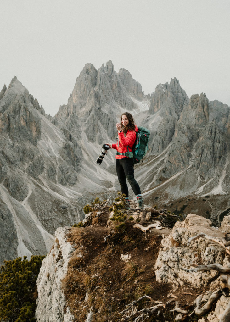 An elopement photographer in the Italian Dolomites stands holding a large camera with the famous peaks of Cadini di Misurina behind her.