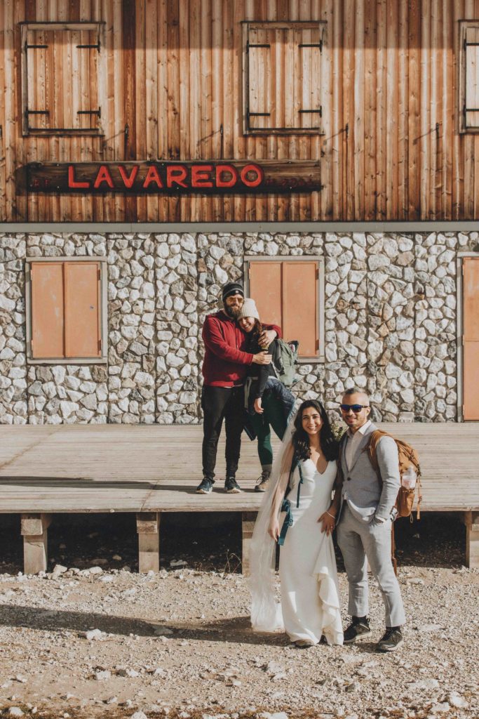 This is an image of a wedding couple and their friends standing near the Lavaredo hut during their two day Dolomites hiking elopement. They are standing in pairs smiling at the camera with the hut behind them.