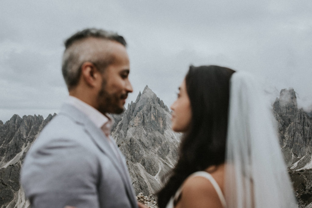 A couple stands near the Cadini di Misurina peaks during their Dolomites elopement. They are facing each other, slightly out of focus with a triangular peak framed in the background between them.