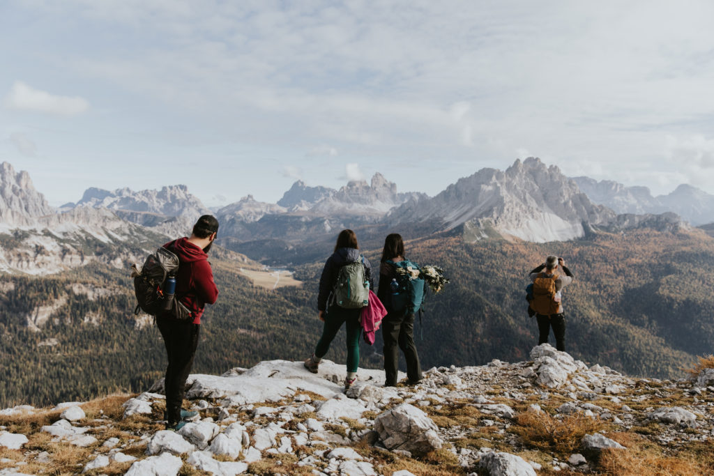 This is a photo of a group of people standing near an overlook on the Lago di Sorapis trail in the Italian Dolomites. They are all facing away toward the valley, wearing hiking clothes and backpacks.
