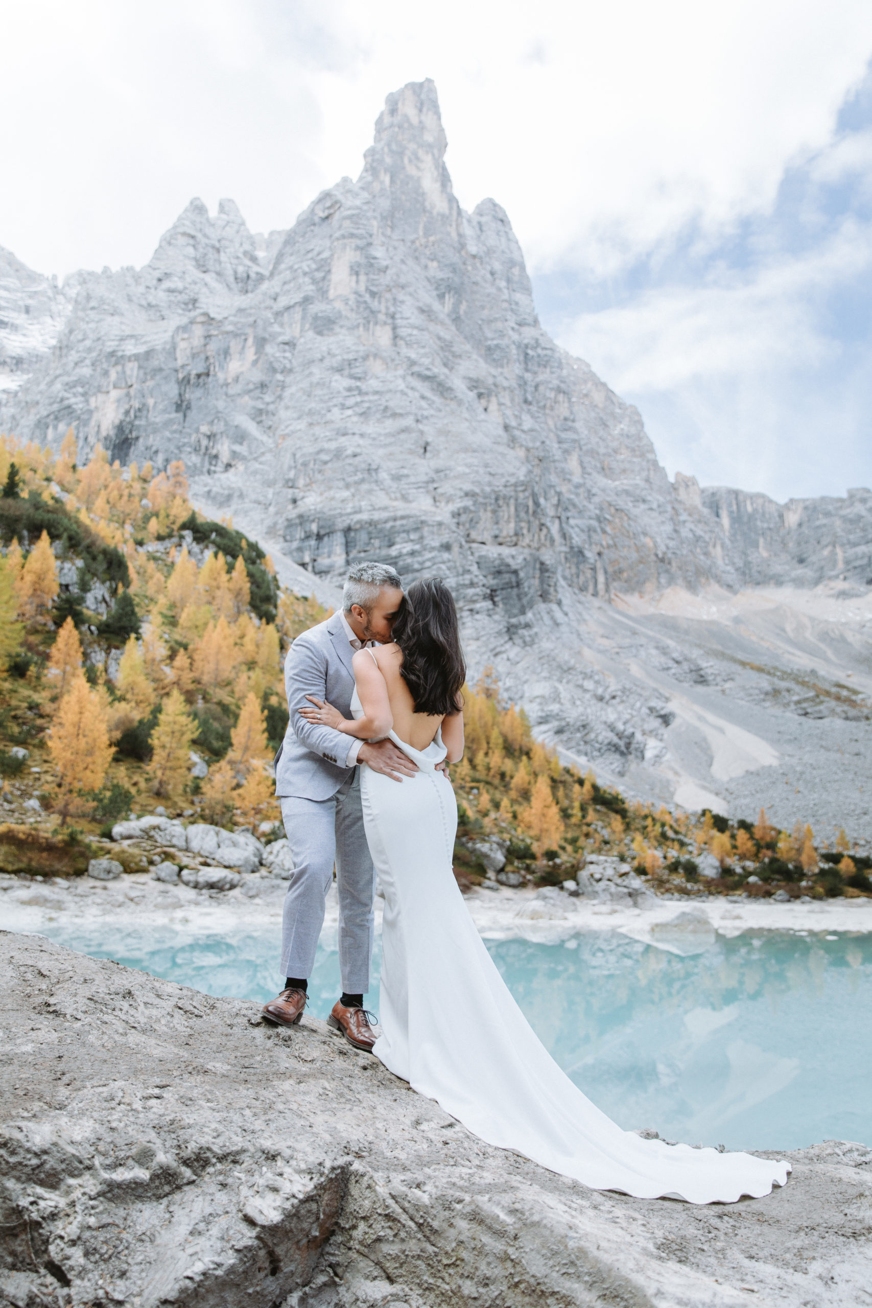 A couple embraces while wearing their wedding attire near the impressive peak over Lago di Sorapis during their Dolomites elopement.