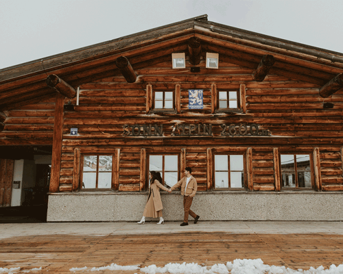 A couple walks past a mountain hut on their elopement day holding hands.