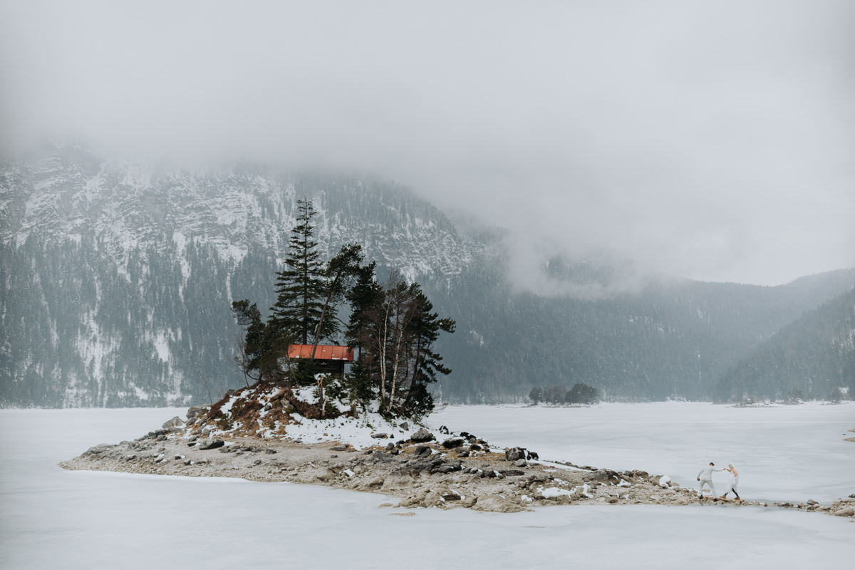 A small hut sits on an islet in the middle of a frozen mountain lake, snowy and isolated.