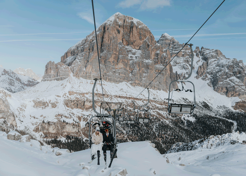 A couple in their wedding attire rides a gondola up to a mountain hut for their ski elopement.
