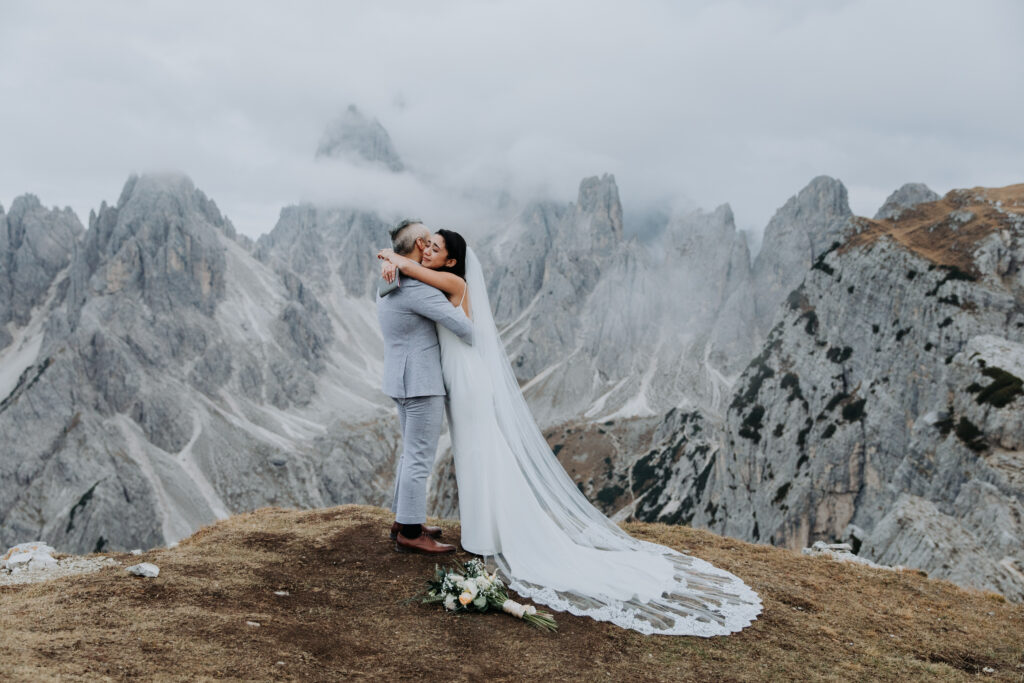 A couple in wedding attire stand near the impressive Cadini di Misurina mountain viewpoint in an emotional embrace after reading their vows.