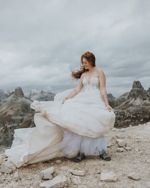 A woman in a wedding dress spins in the wind, her hair and gown blowing wildly, during her Tre Cime elopement