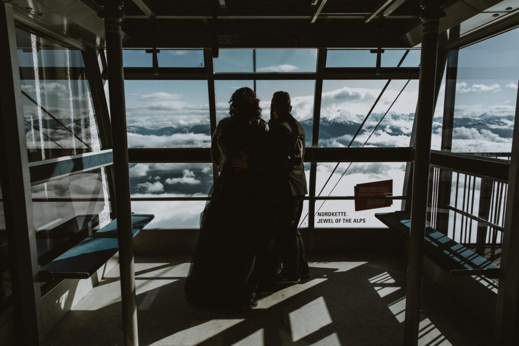 A couple eloping in Innsbruck stand on the Norkette cable car with a view of the mountains in the distance.