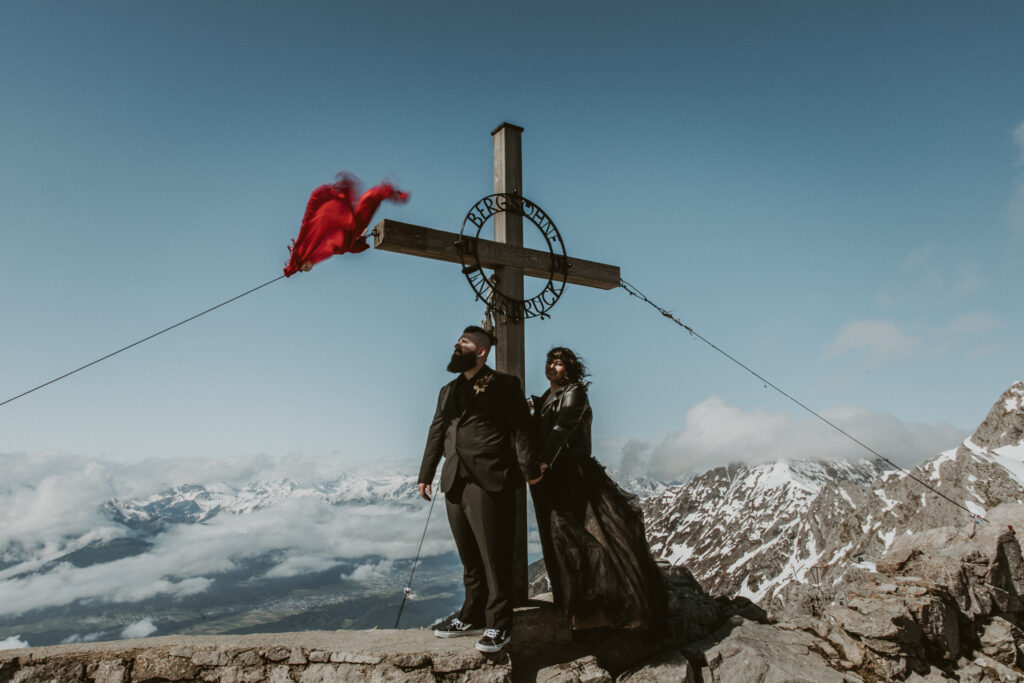 A couple stands on top of the Nordkette mountain chain during their innsbruck elopement. They are wearing all black wedding attire.
