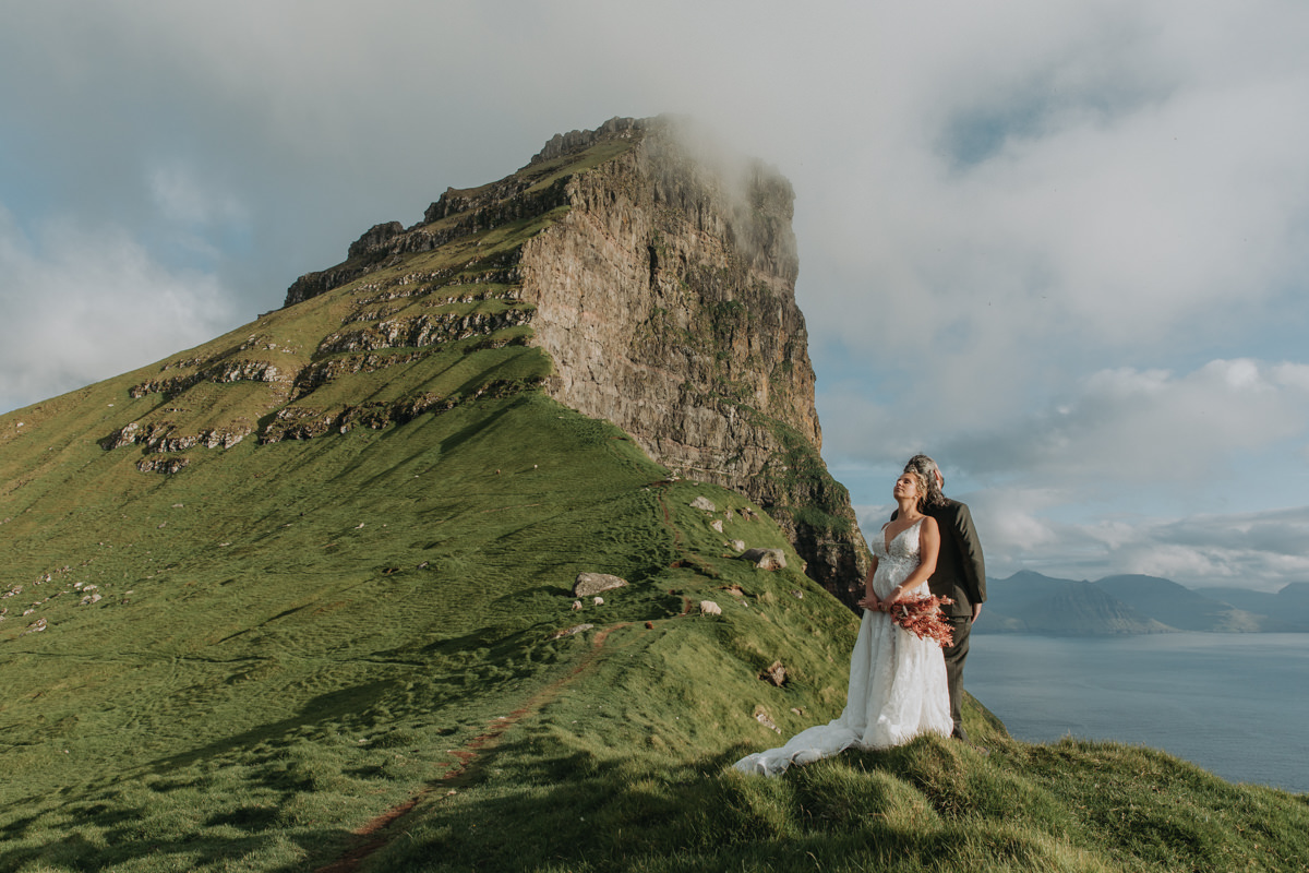 A couple stands near a cliff on the Faroe Islands during their elopement day on Kalsoy, near the Kallur lighthouse.