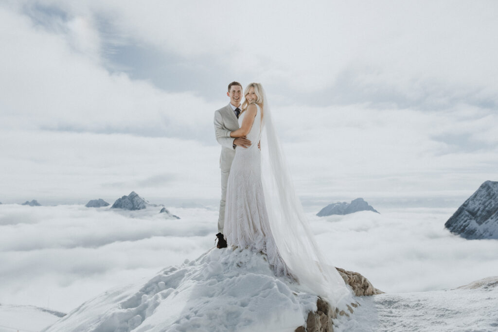 A couple stand on a glacier in Austria wearing their wedding clothes, with snow and mountains spreading in the distance.