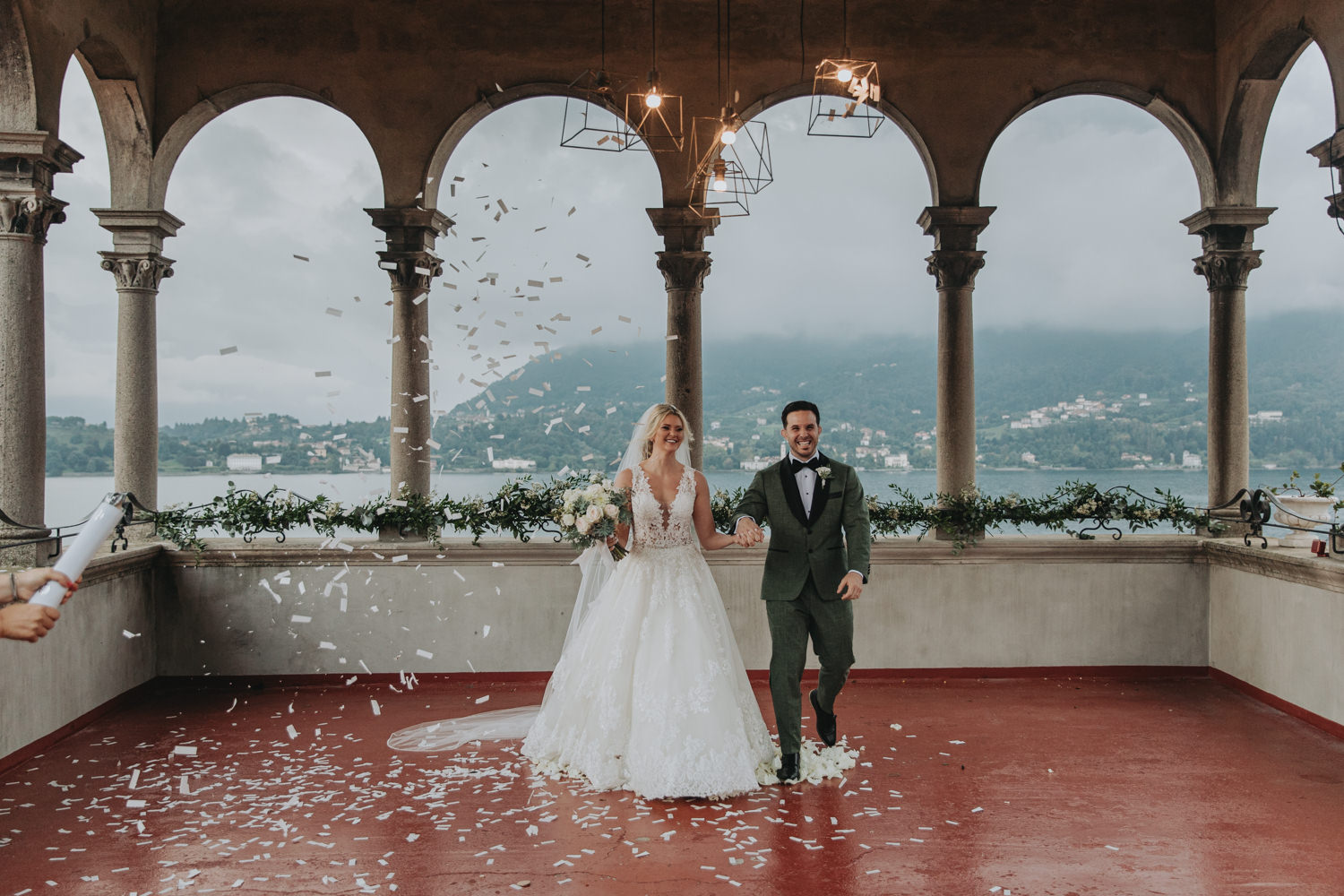 A couple walk smiling toward the camera through confetti after their elopement wedding ceremony along Lake Como