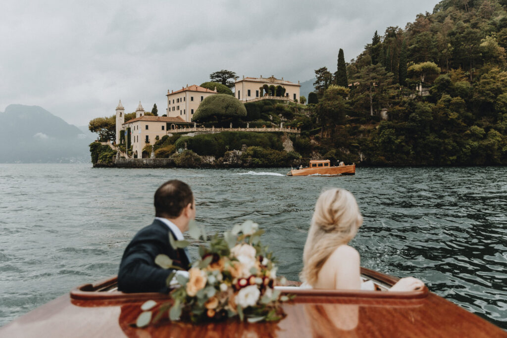 A couple on their lake como boat elopement looks toward Villa Balbianello on an overcast day