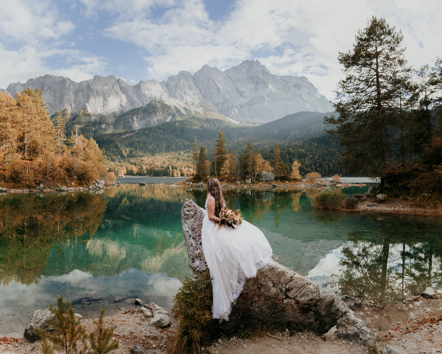 A bride looks toward the Zugspitze during her elopement on the Bavarian lake of Eibsee on colorful autumn day