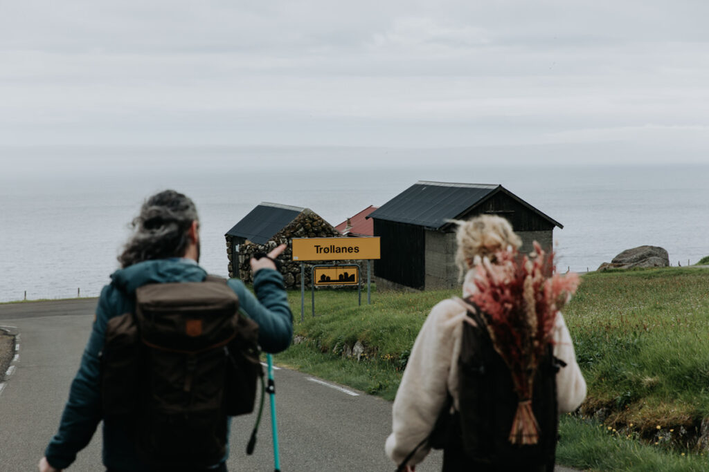 A couple wearing hiking clothes walks toward Trollanes, a small village in the Faroe Islands