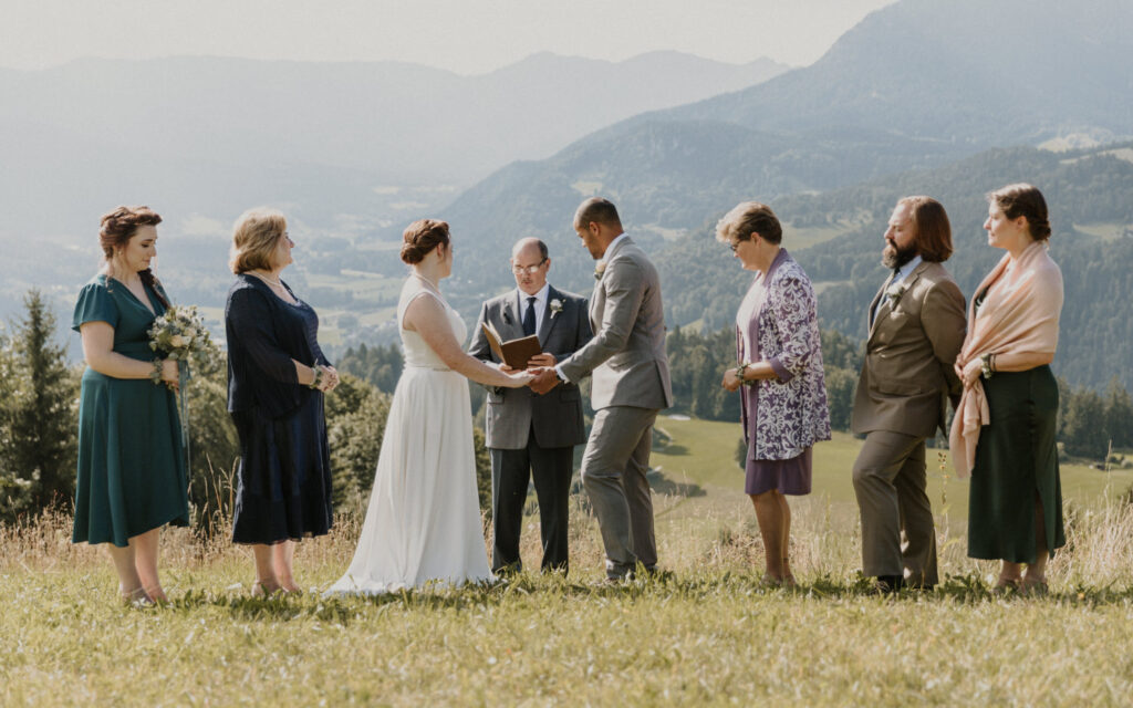 A group of friends and family stand around a couple holding hands on a grassy mountain during their minimony elopement ceremony
