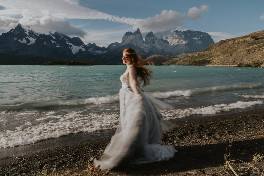 A woman with red hair twirls in the wind in front of Lake Pehoe during her elopement day in Patagonia.