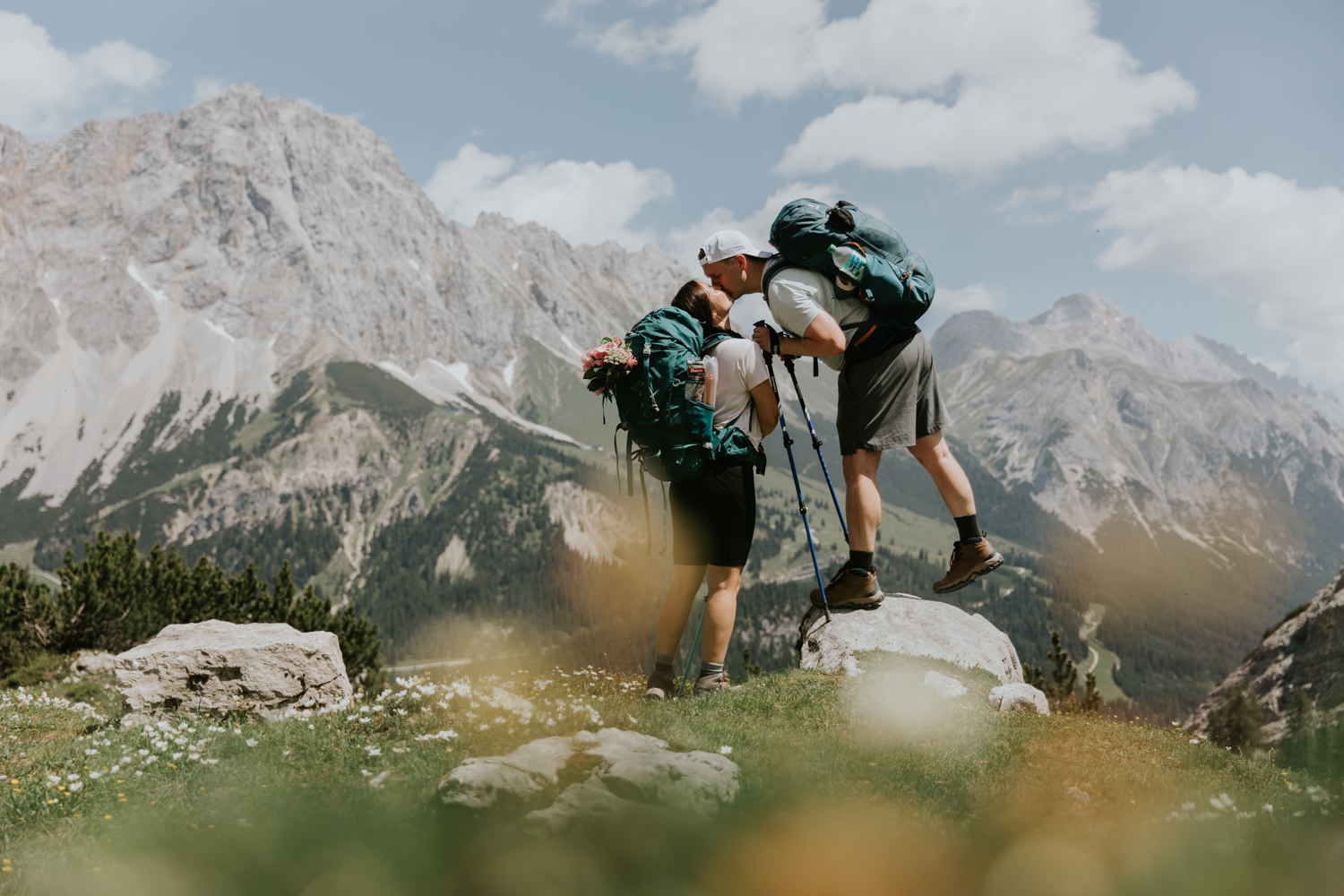 A couple in hiking clothes stands kissing in front of an alpine landscape during their couple's photo session