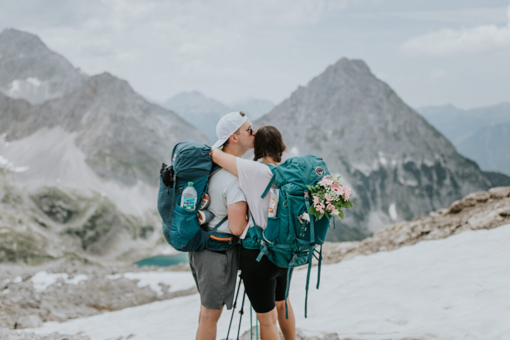 A couple hiking on their elopement day hug near the Austrian Zugspitze, framed by melting snow and tall rocky cliffs.