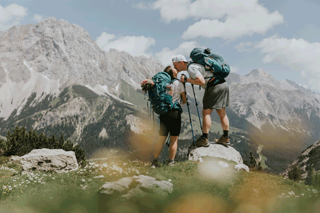 A couple hiking on their elopement day kiss under the Austrian Zugspitze, framed by yellow wildflowers.