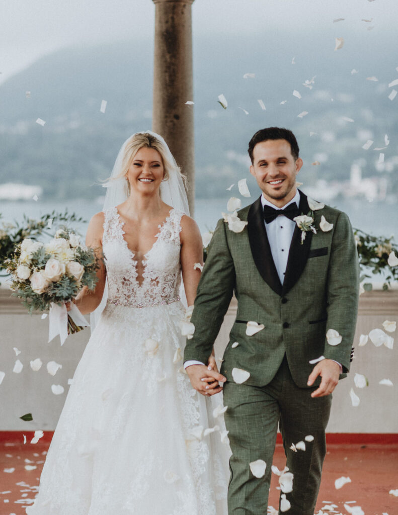 A couple walk toward the camera smiling through rose petals on the roof of a villa as they celebrate their lake Como elopement.