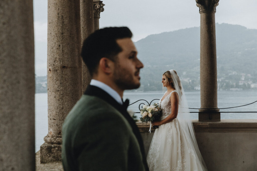 A couple in white wedding dress and dark green suit stand facing each other under an Italian villa on Lake Como during their wedding day.