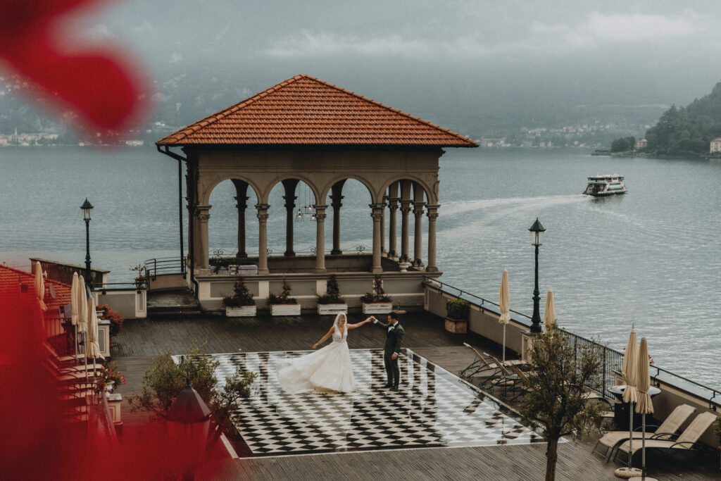A couple in wedding dress and suit stand far away from the camera, dancing on the checkered dance floor atop Grand Hotel Cadenabbia on a moody fall day