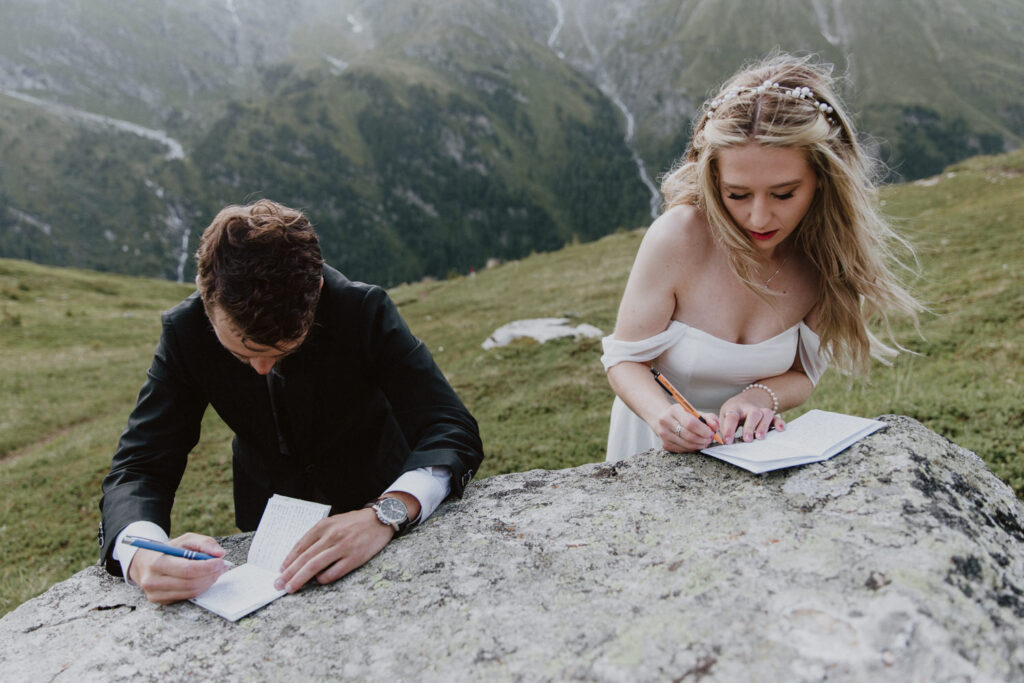 A couple are writing their wedding vows on a large boulder. They are wearing wedding clothes for their summer hiking elopement in Austria.