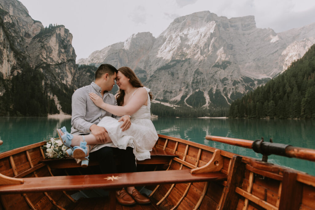 A couple snuggle on a wooden boat on Lago di Braies with the impressive Italian Dolomites in the background.