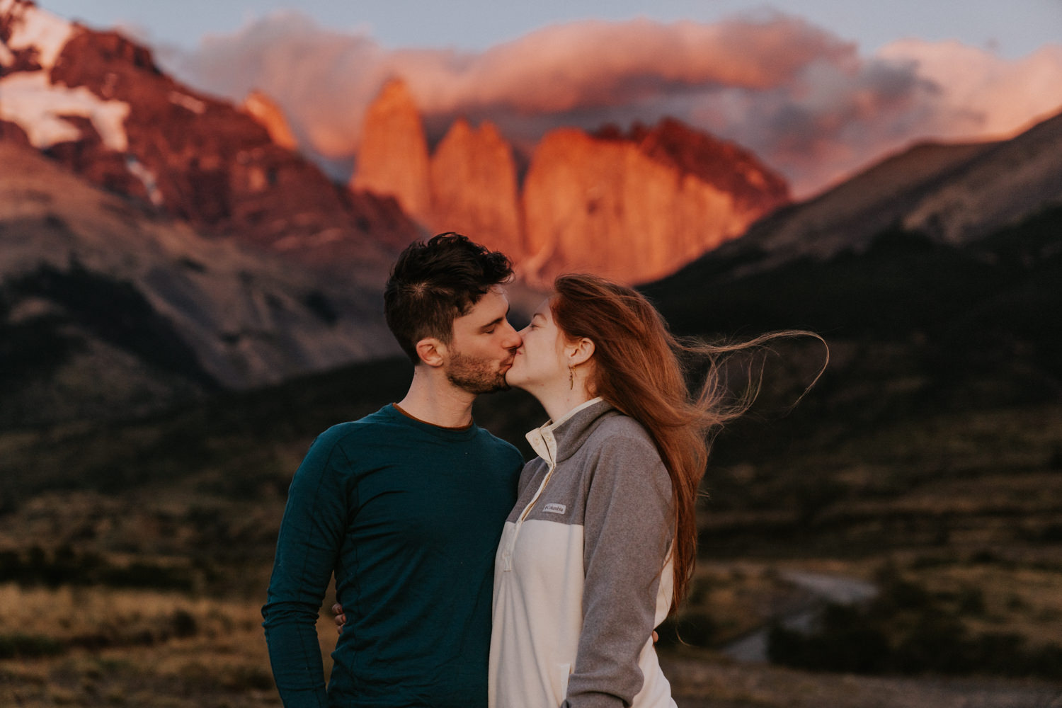 A couple kiss in front of a bright pink Torres del Paine, light by the sunrise alpine glow during their Patagonia elopement.