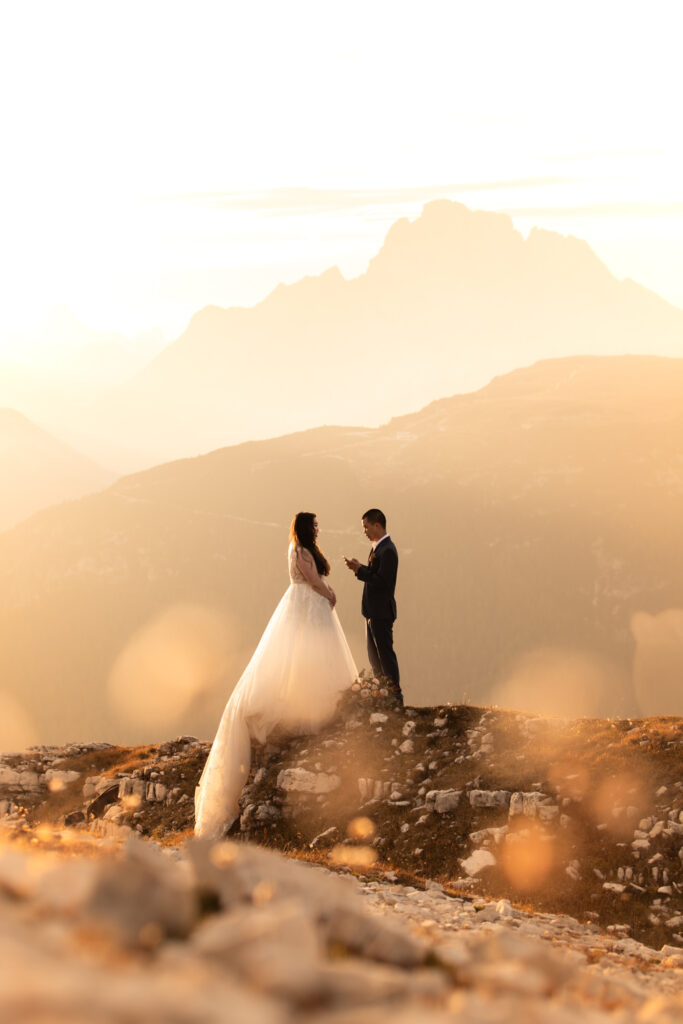 A couple in wedding dress and suit pose for elopement photos in the Dolomites, during a golden sunset reading vows.