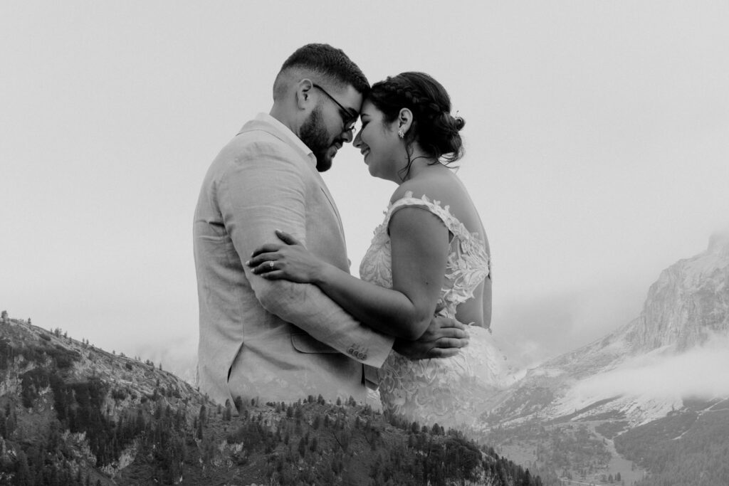 A black and white double exposure of a wedding couple touching foreheads with the summer landscape of the Italian Dolomites in July framing them.