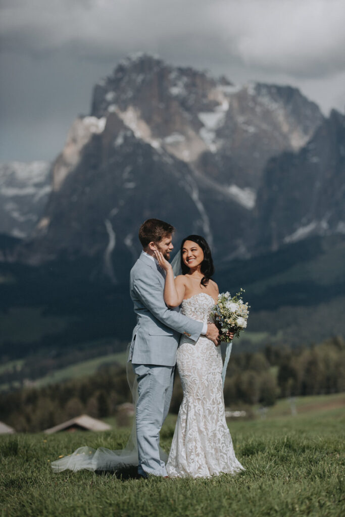 A couple pose for their elopement photos at Alpe di Suisi in the Italian Dolomites. They are standing in an embrace, with snow capped mountains far in the distance.