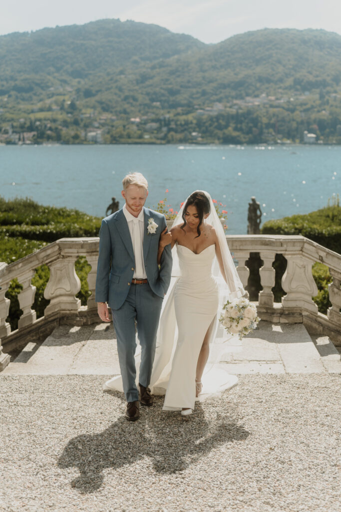 A mixed race couple in wedding attire walk on the grounds of Villa Carlotta, Lake Como, Italy, during their wedding day